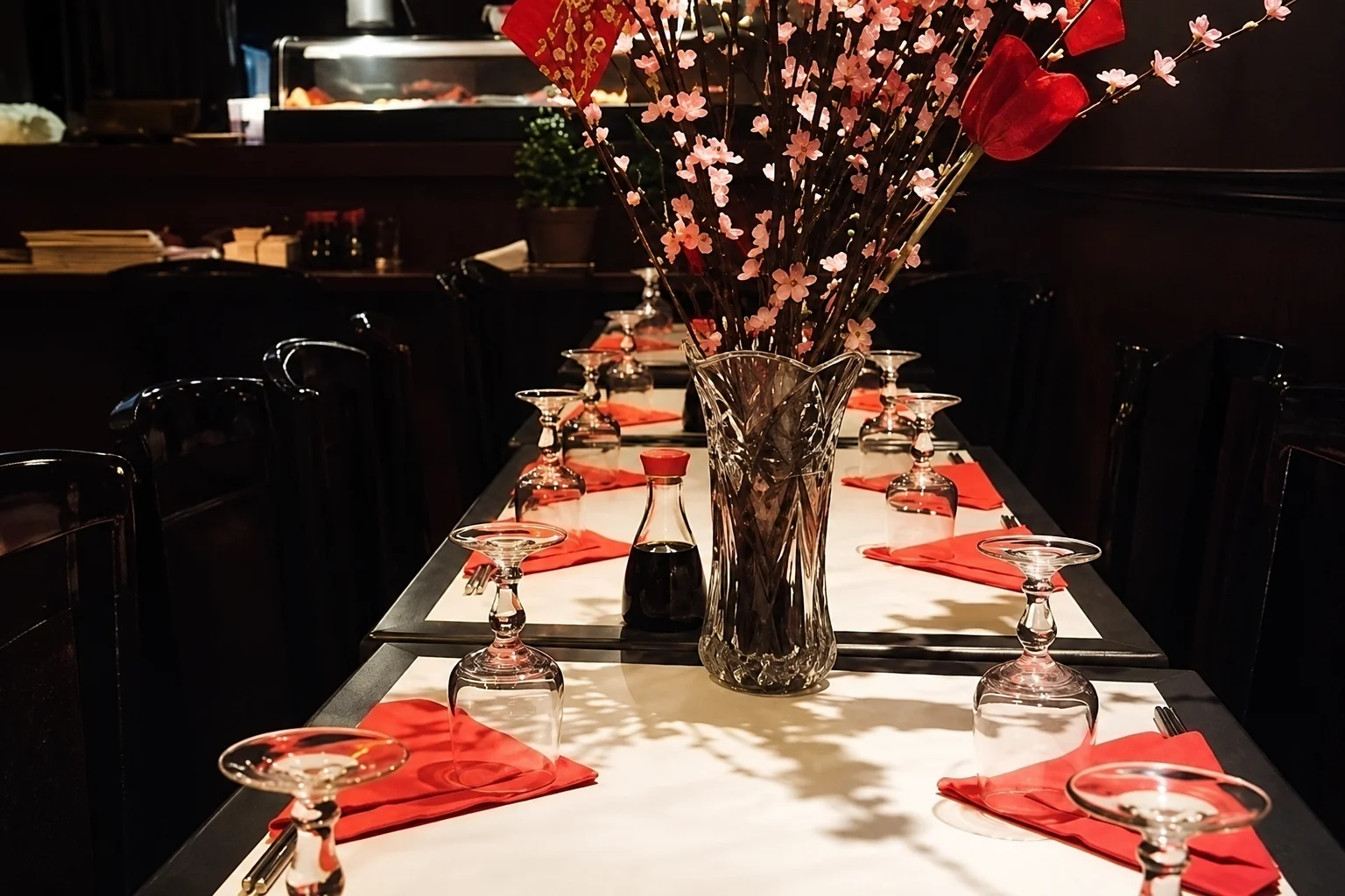Set table with upturned glasses, red napkins, soy sauce and a vase of flowering branches.